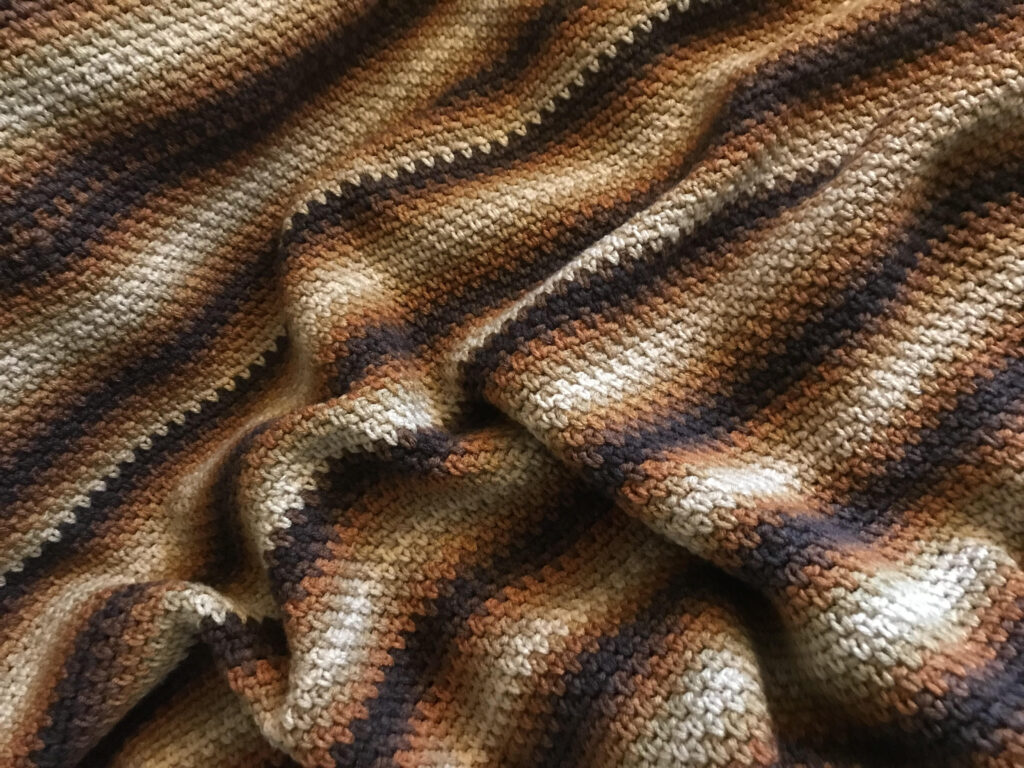 An up close image of a crocheted afghan in a variety of brown tones.