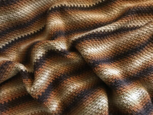 An up close image of a crocheted afghan in a variety of brown tones.