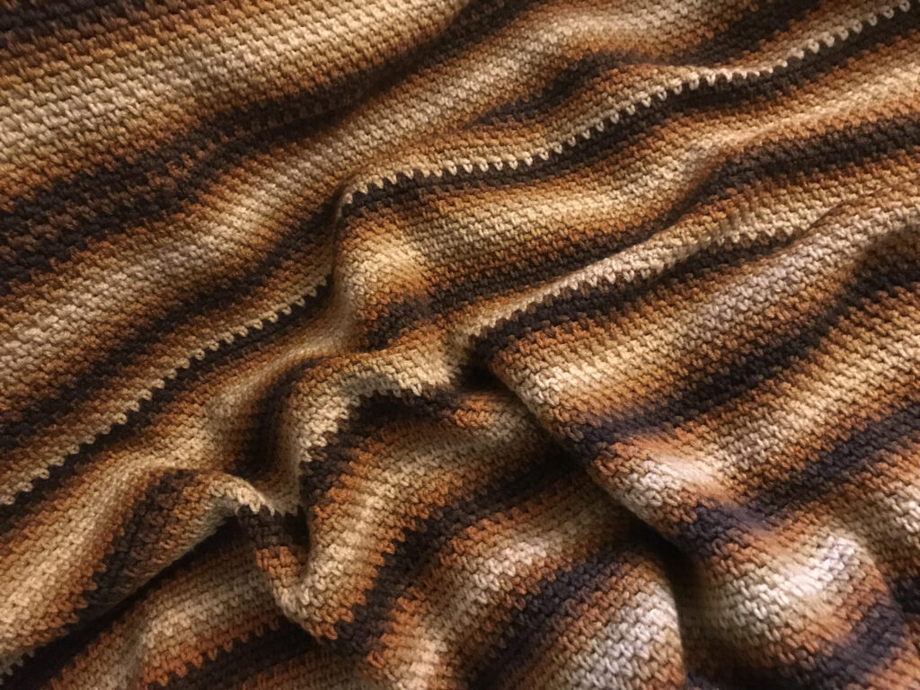An up close image of a crocheted afghan in a variety of brown tones.